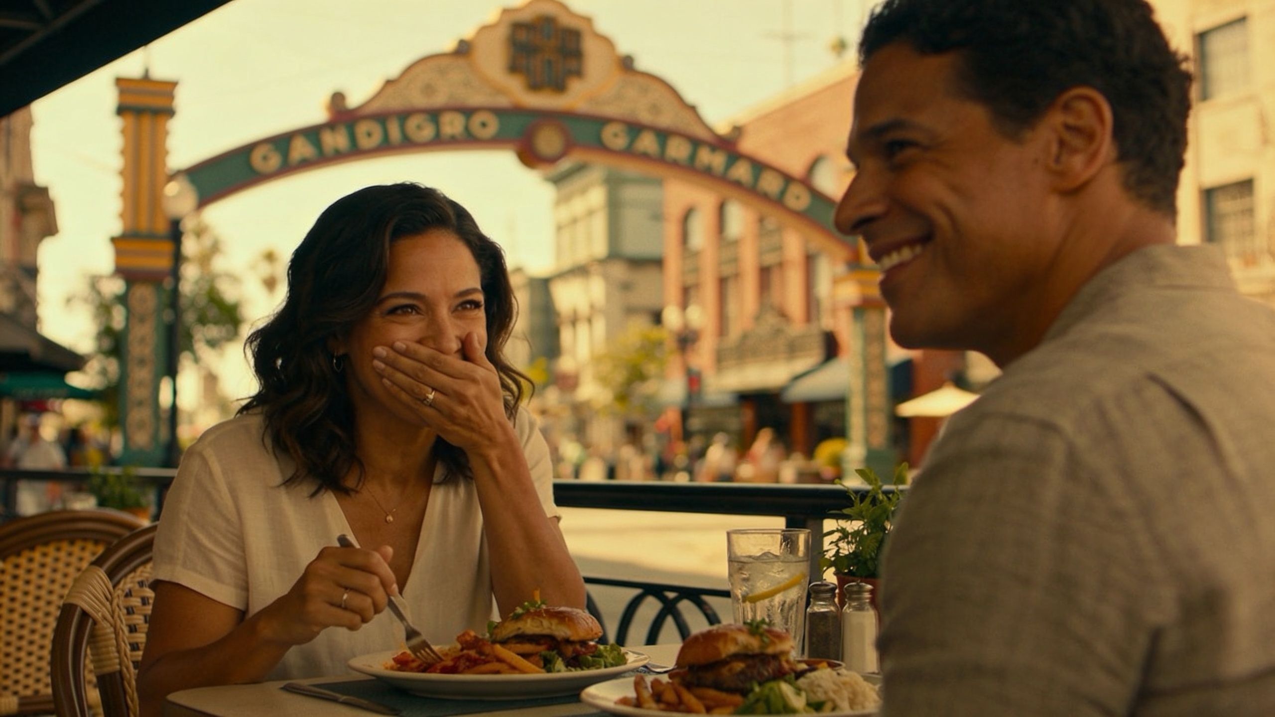 A happy couple enjoying a meal together at an outdoor restaurant with a decorative archway in the background.