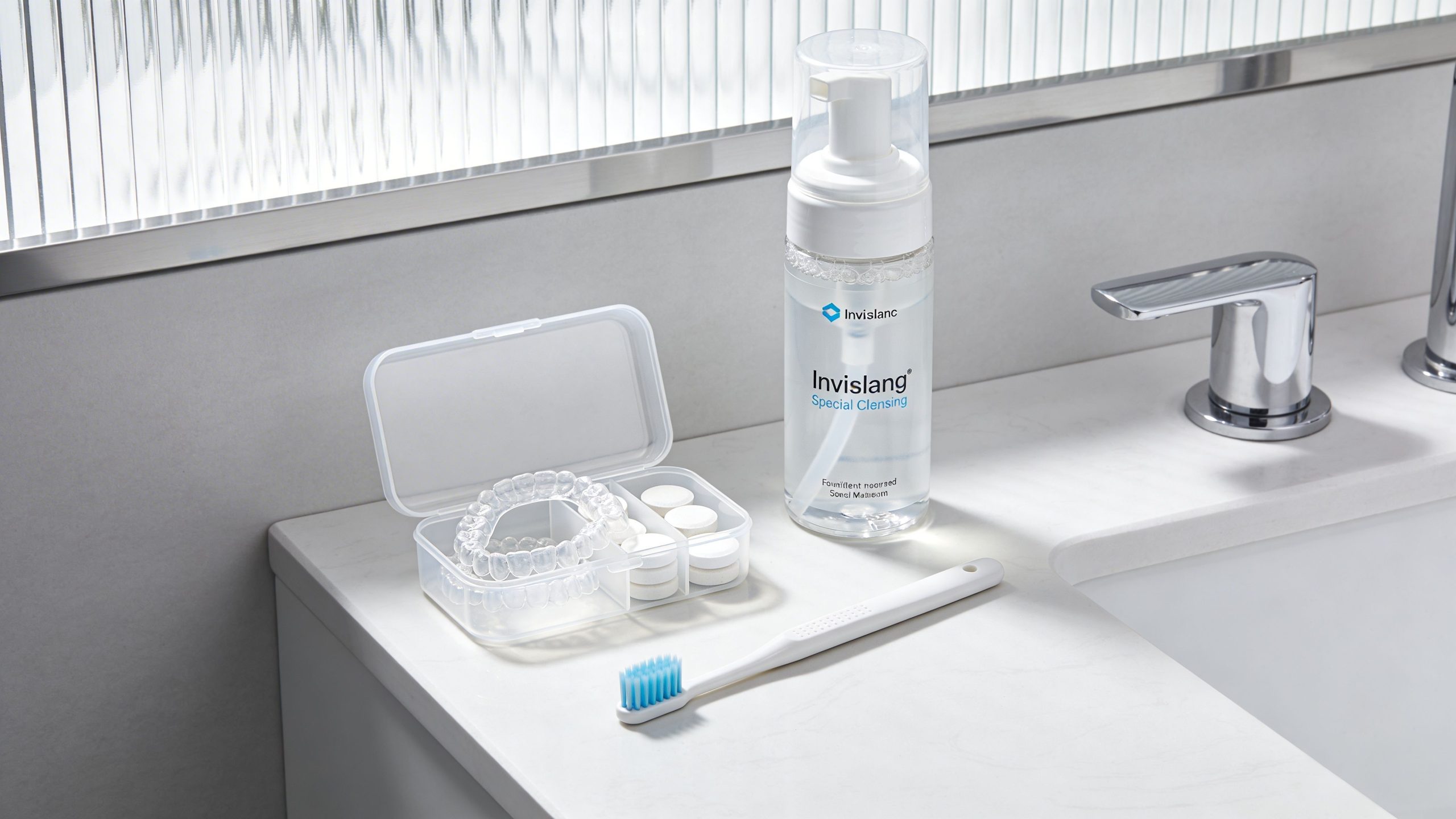 An Invisalign cleaning kit with clear aligners, cleaning tablets, a bottle of foam cleanser, and a toothbrush.
